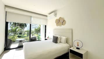 A bedroom with a large bed, a bedside table, a wall-mounted air conditioner, and a view of the outdoors.