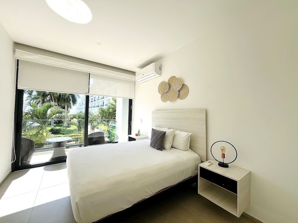 Un dormitorio con una cama grande, una mesita de noche, aire acondicionado instalado en la pared y vistas al exterior.