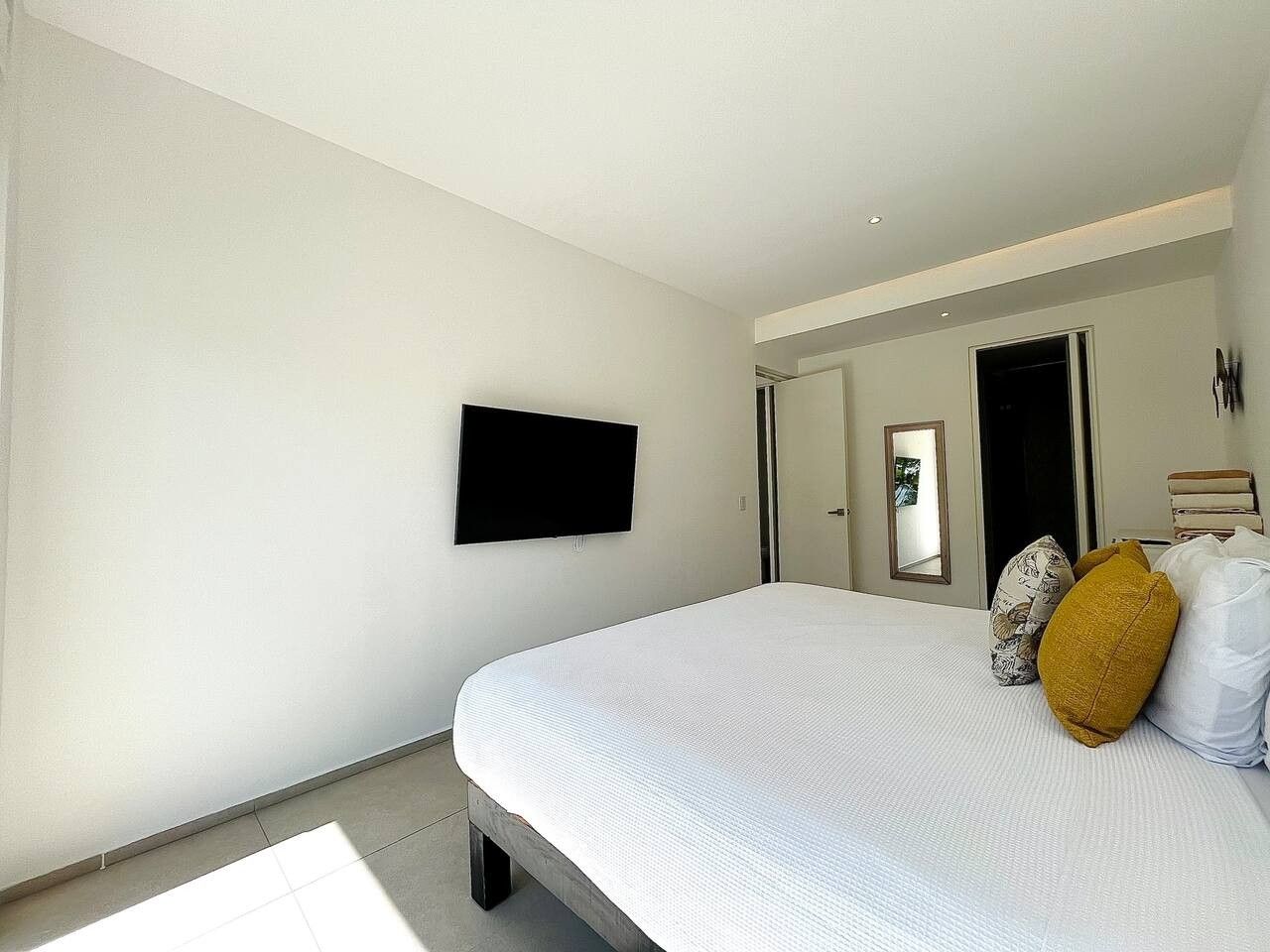 Une chambre à coucher comprenant un lit, un téléviseur à écran plat fixé au mur et une porte donnant sur une autre pièce.