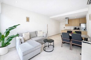 Una sala de estar moderna con un sofá seccional gris, una mesita redonda y un comedor con una mesa y sillas de madera.