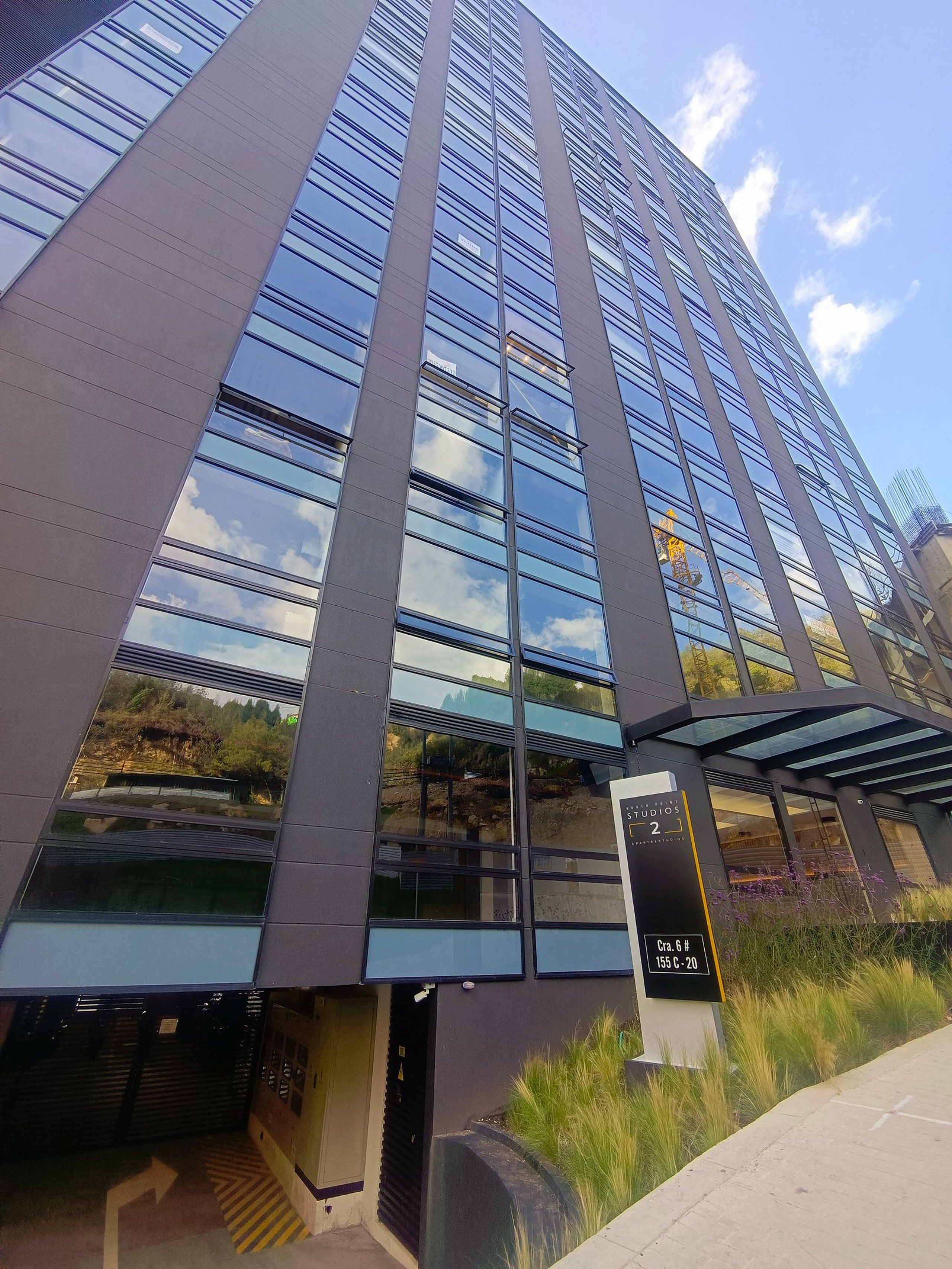A modern building with reflective glass windows and a sign indicating 'Studios 2' and 'Cra. 6 # 155 C. 20'.