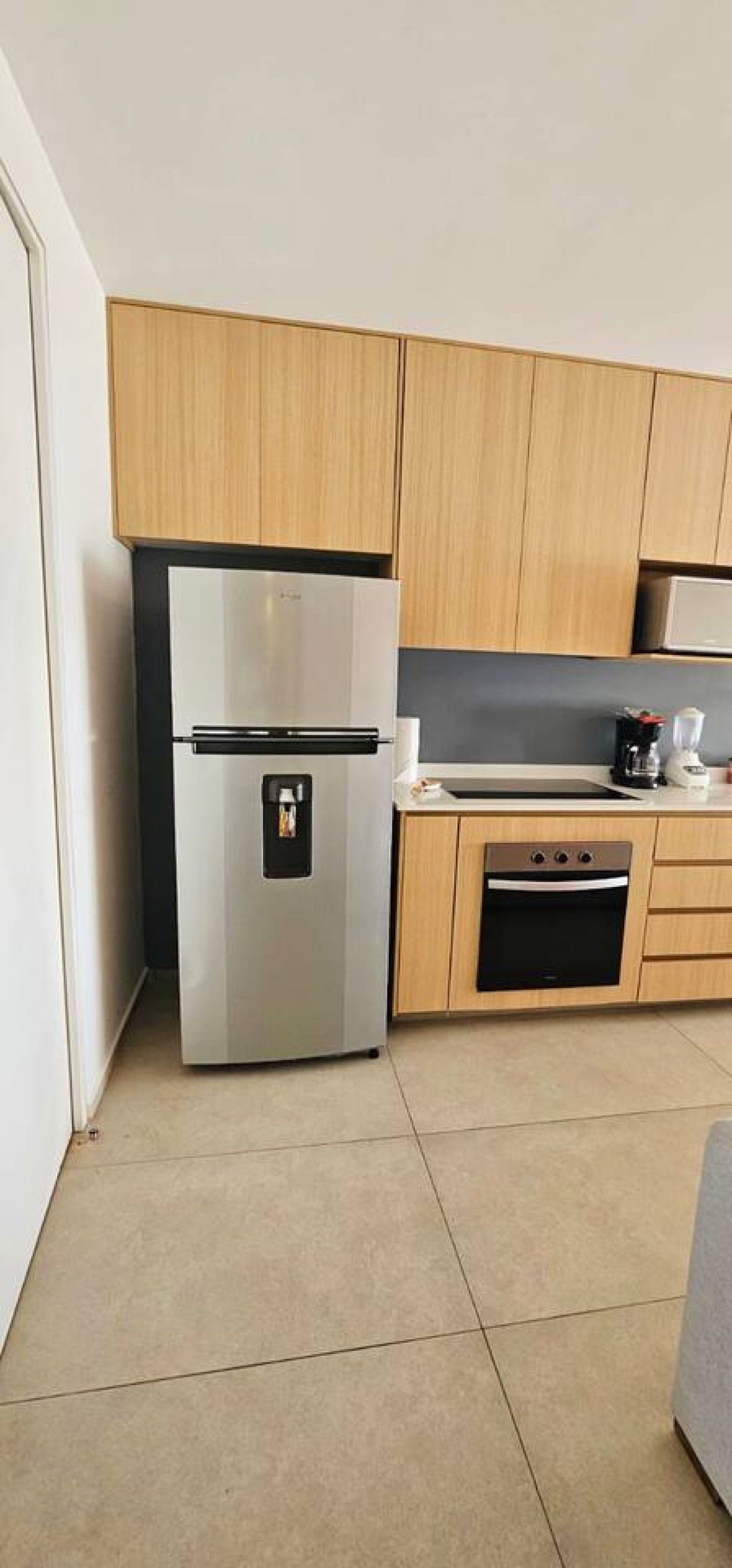 A compact kitchen with a stainless steel refrigerator, wooden cabinets, a built-in oven, and a countertop with a coffee maker.