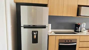 A compact kitchen with a stainless steel refrigerator, wooden cabinets, a built-in oven, and a countertop with a coffee maker.