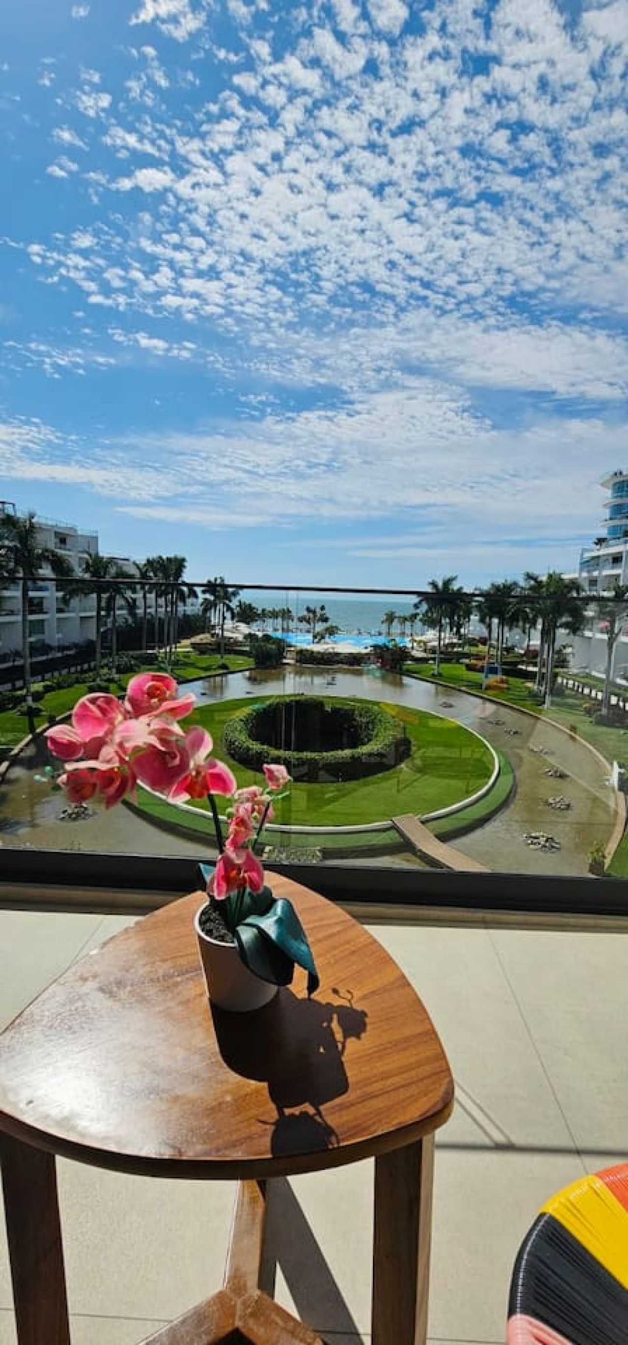 A view from a balcony with a flower arrangement, a circular garden, and a clear sky.