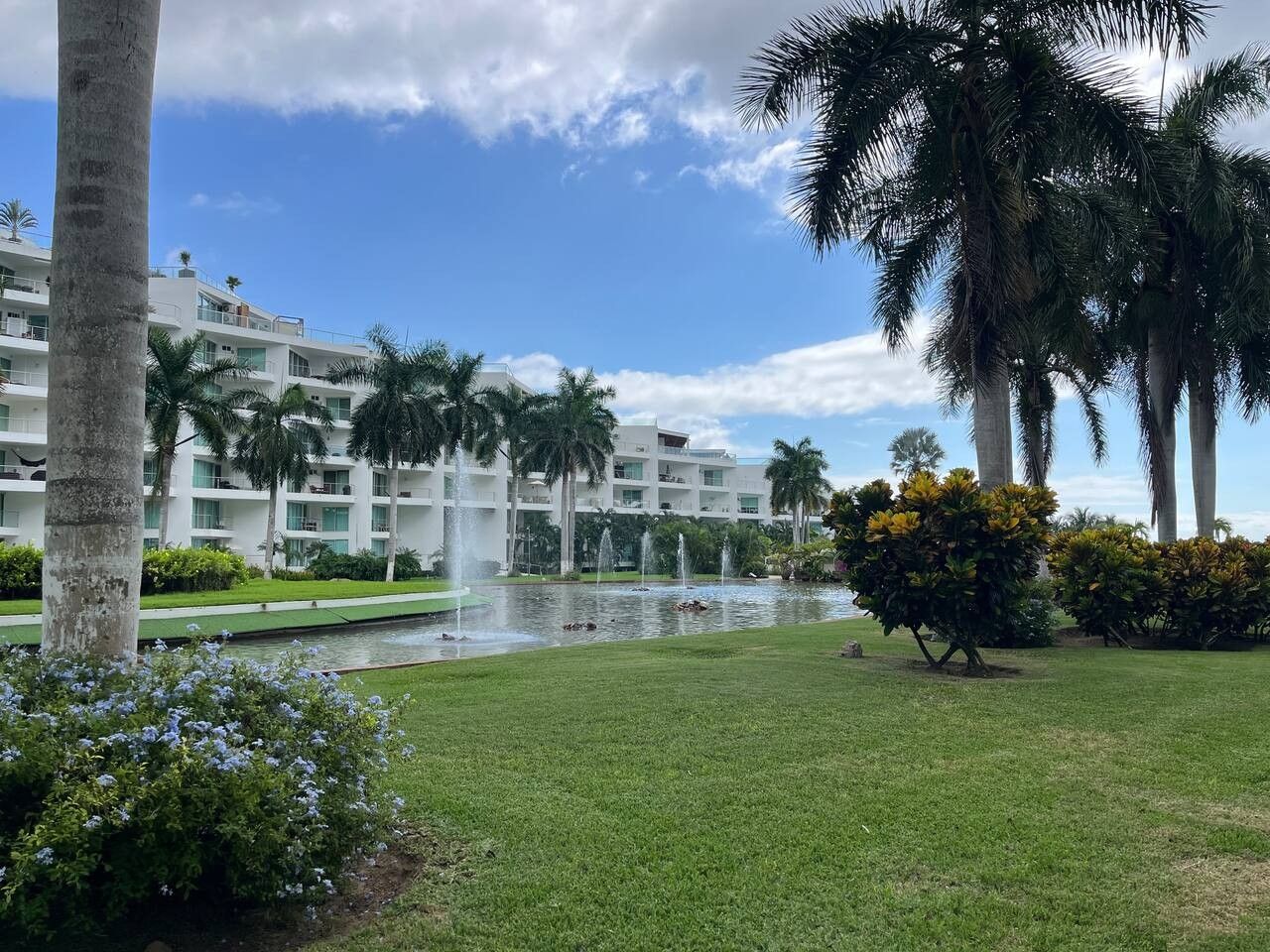 A hotel with a pool, palm trees, and a clear sky.