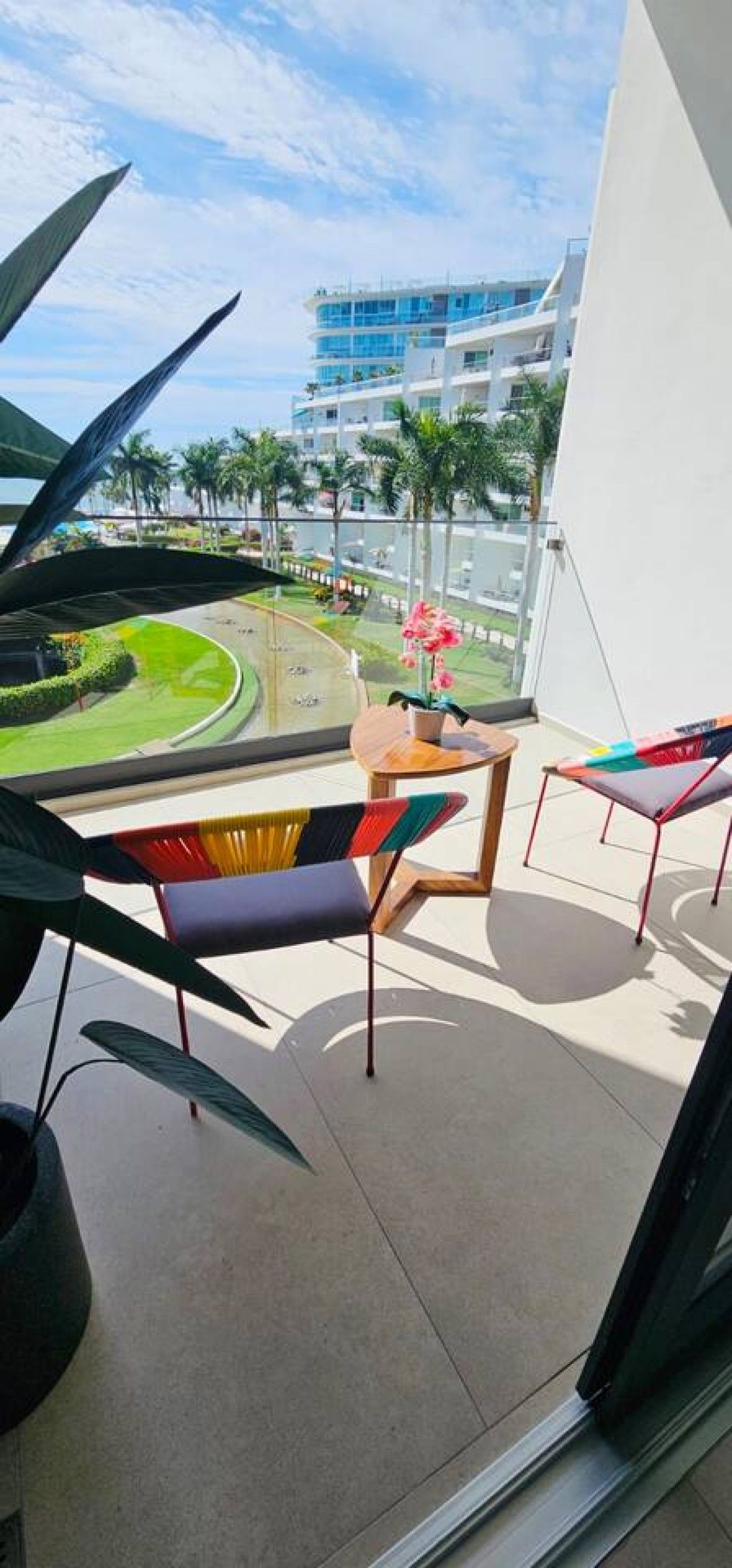 Un balcon donnant sur un immeuble moderne, une table ronde et des chaises colorées.