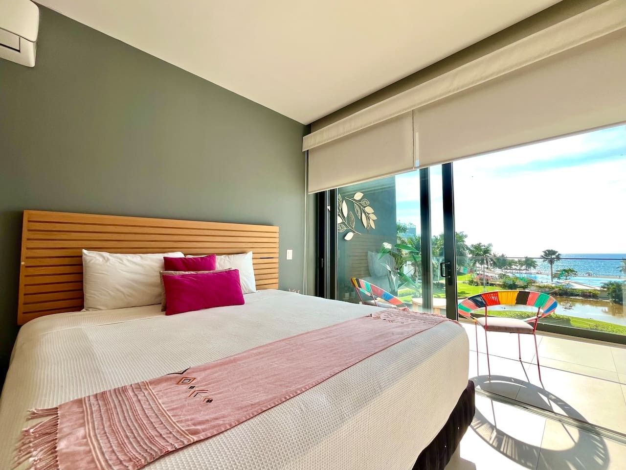 A modern bedroom with a large bed, a view of the ocean, and a balcony with a chair.