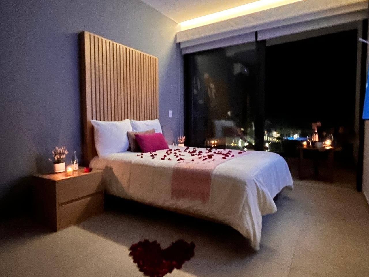 A bedroom with a bed, bedside tables, and a view through a large window.