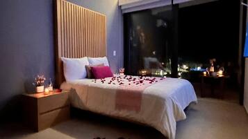 A bedroom with a bed, bedside tables, and a view through a large window.