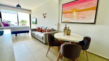 A modern living room with a dining area, a sofa, a TV, and a large painting.