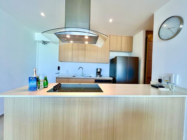 A modern kitchen with a central island, a built-in oven, and a stainless steel refrigerator. - Comodo Penthouse Aria1012 Playa/Albercas Nvo. Vta. (Nuevo Vallarta)