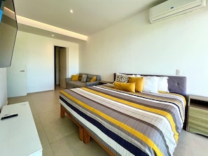 A bedroom with a bed, bedside tables, a television, and an air conditioning unit. - Comodo Penthouse Aria1012 Playa/Albercas Nvo. Vta. (Nuevo Vallarta)