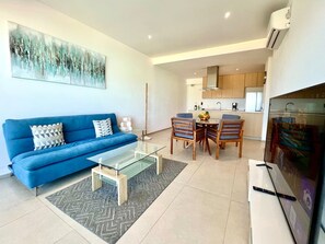 Un salon moderne avec un canapé bleu, une table basse en verre et un coin repas avec des chaises en bois.