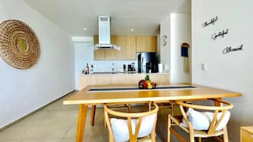 Cozinha moderna com armários de madeira, geladeira de aço inoxidável e uma mesa de jantar com duas cadeiras.
