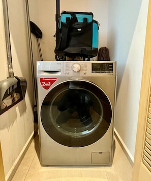 Un lave-linge à chargement frontal doté d’un panneau de commande, d’un autocollant rouge et d’un sac bleu posé sur le dessus.