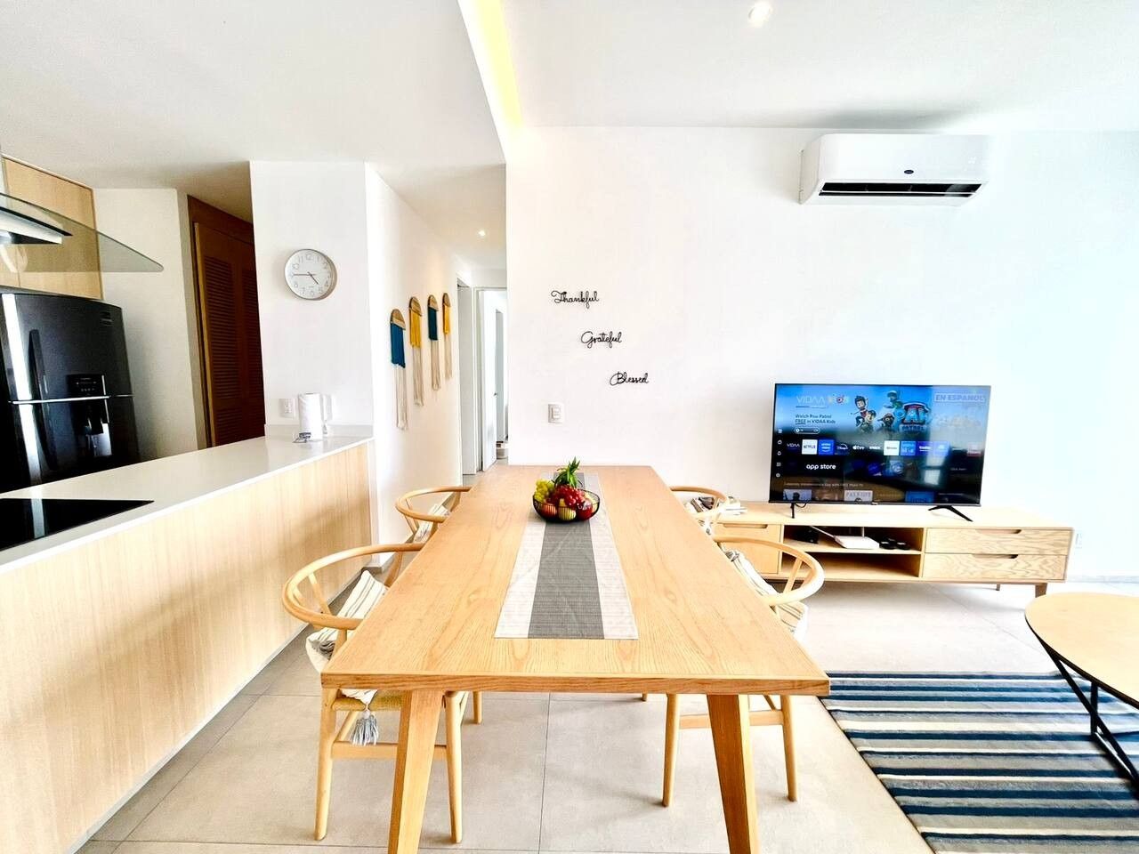 A modern kitchen with a built-in stove, a dining area with a wooden table and chairs, and a television on a stand.