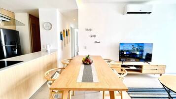 A modern kitchen with a built-in stove, a dining area with a wooden table and chairs, and a television on a stand.