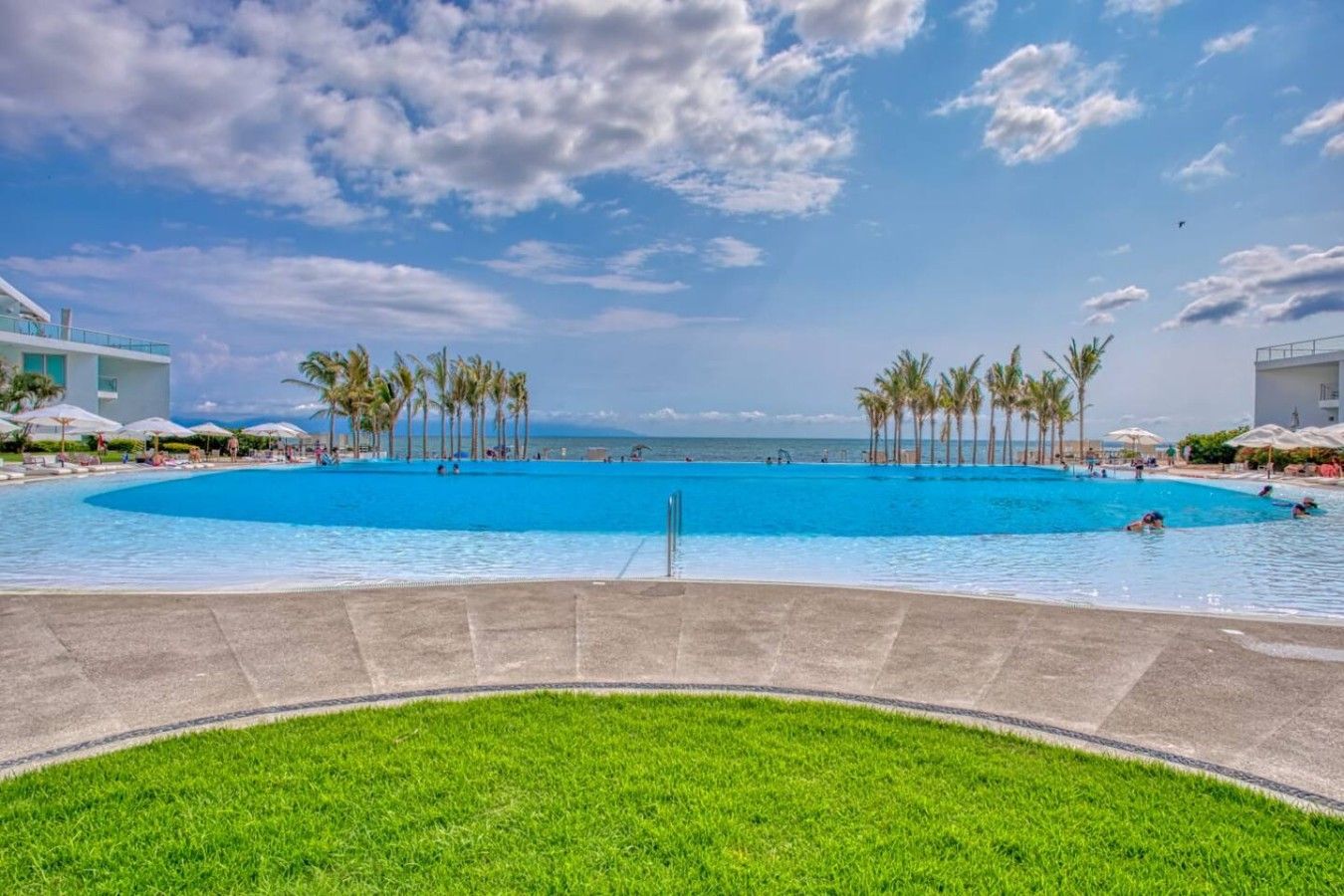 A large outdoor swimming pool with palm trees and a clear sky.