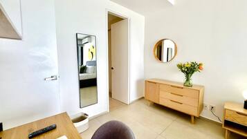 Une chambre moderne avec un bureau en bois, une chaise, une table de chevet, une commode et un miroir au mur.