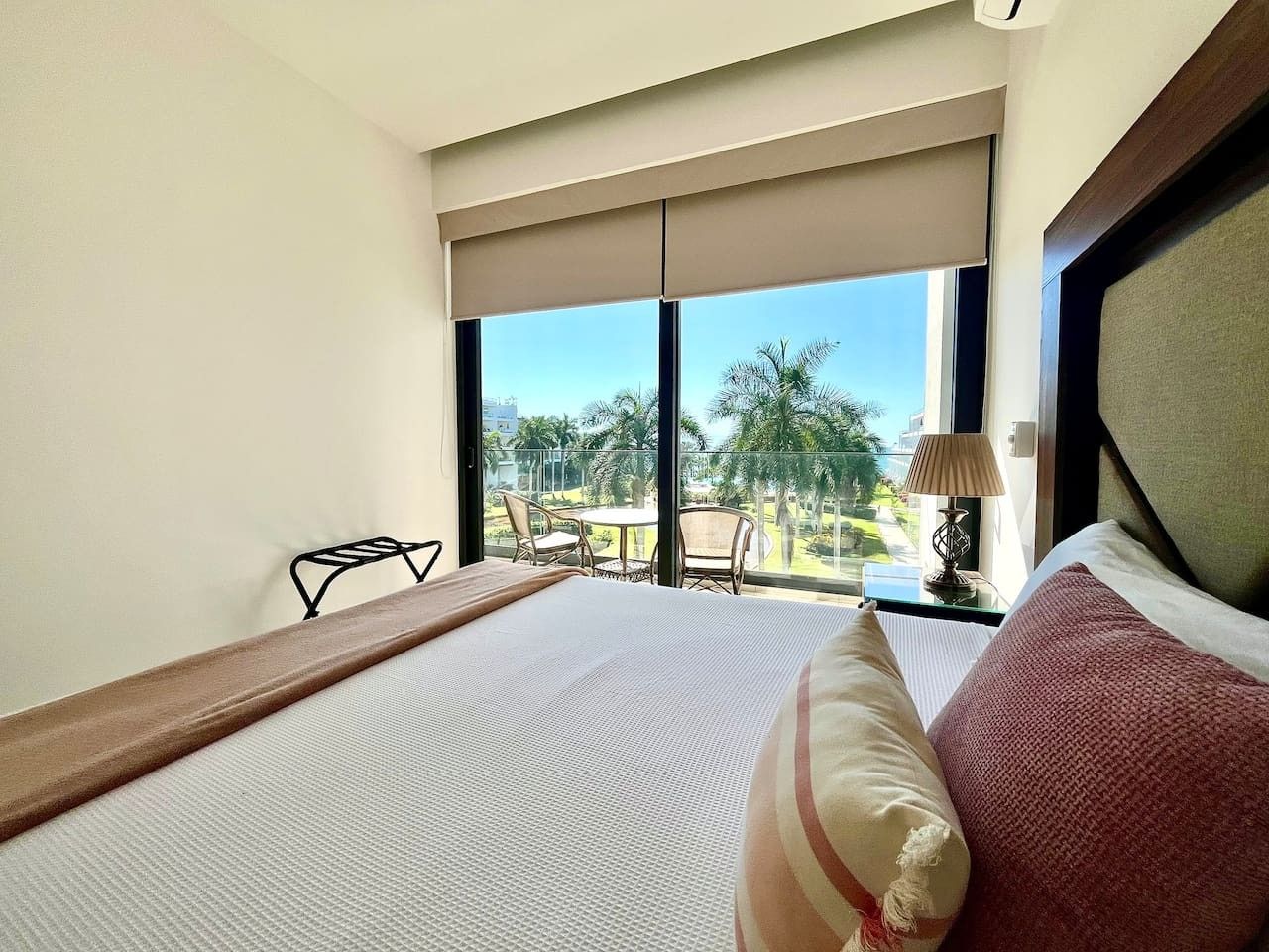 Une chambre d’hôtel avec un grand lit, une vue sur les palmiers et un balcon équipé de chaises.