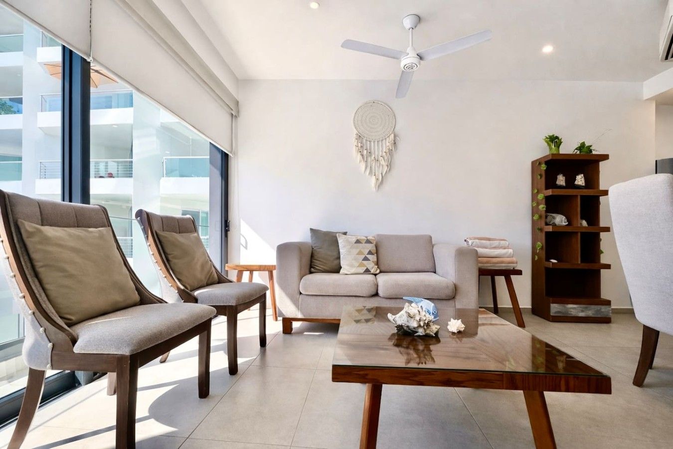 A modern living room with a sofa, two armchairs, a coffee table, a bookshelf, and a ceiling fan.