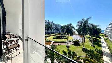 Un balcone con vista su un giardino curato, palme e uno specchio d'acqua.