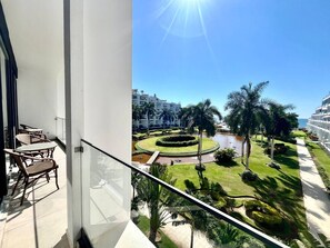 Un balcone con vista su un giardino curato, palme e uno specchio d'acqua.