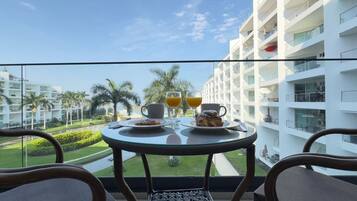 Un balcon avec une table dressée pour le petit-déjeuner, donnant sur un immeuble moderne et un espace paysager agrémenté de palmiers.