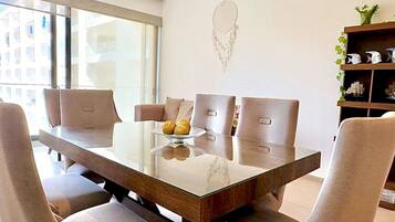 Uma zona de refeições moderna com mesa de vidro, cadeiras estofadas e um painel decorativo.
