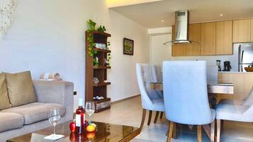 A modern living room with a sofa, a glass coffee table, and a dining area with chairs and a table.