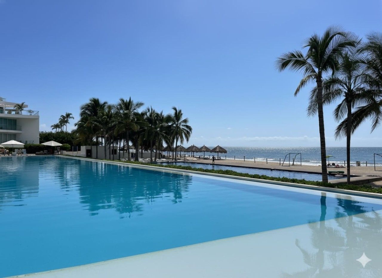A clear blue pool with a view of the beach and palm trees.