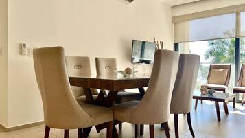 A dining area with a glass table, four chairs, and a television.