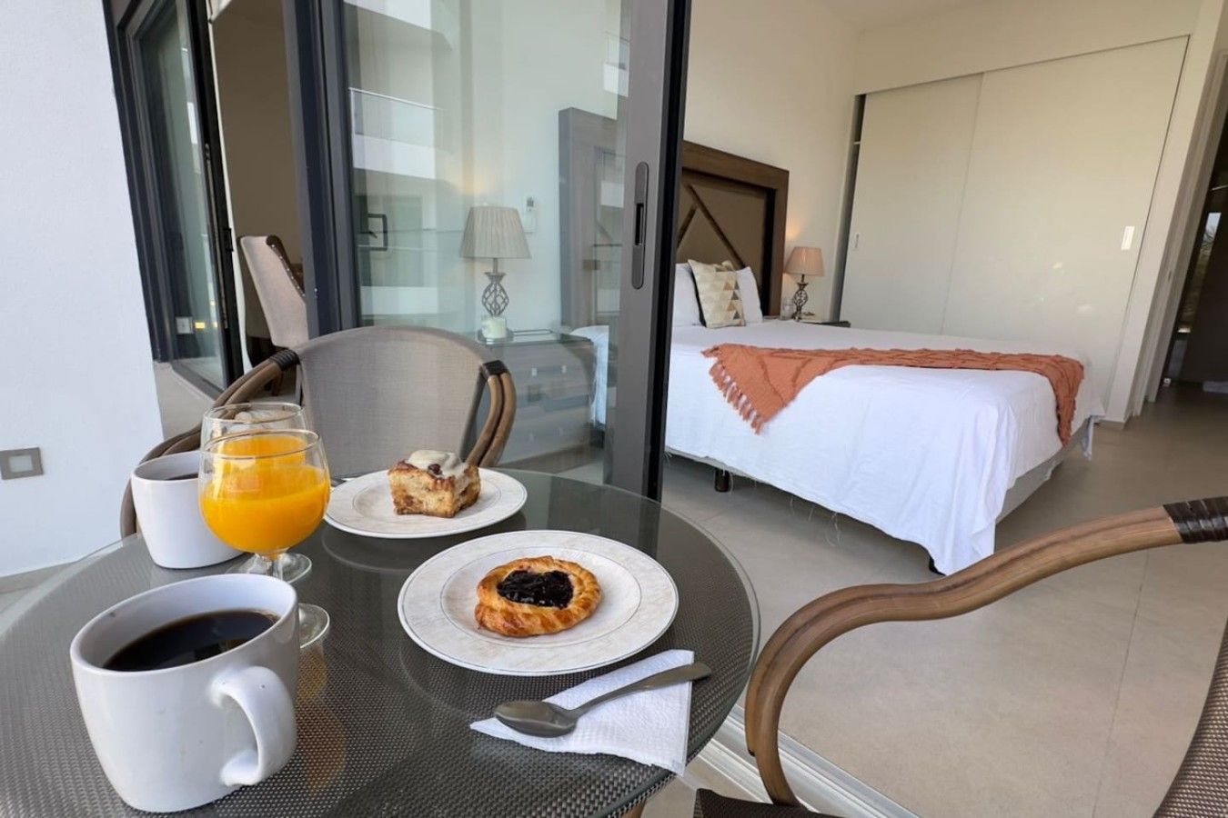 Een hotelkamer met een bed, een eettafel met ontbijtartikelen en een glas sinaasappelsap.