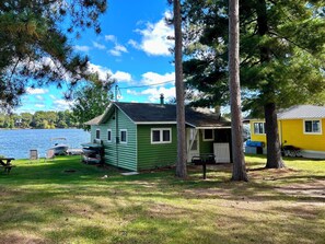 A green cabin with a dock and chairs by a lake. - Charming Renovated Northwoods Cabin on Chetek Chain of Lakes (Chetek)
