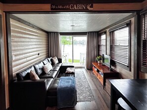 A cabin interior with a sofa, ottoman, TV stand, and a sign above the door. - Charming Renovated Northwoods Cabin on Chetek Chain of Lakes (Chetek)