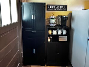 A kitchen area with a coffee bar setup including a Keurig coffee maker, a coffee mug, and a coffee pot. There is a cabinet with two drawers and a shelf with various kitchen items. - Charming Renovated Northwoods Cabin on Chetek Chain of Lakes (Chetek)