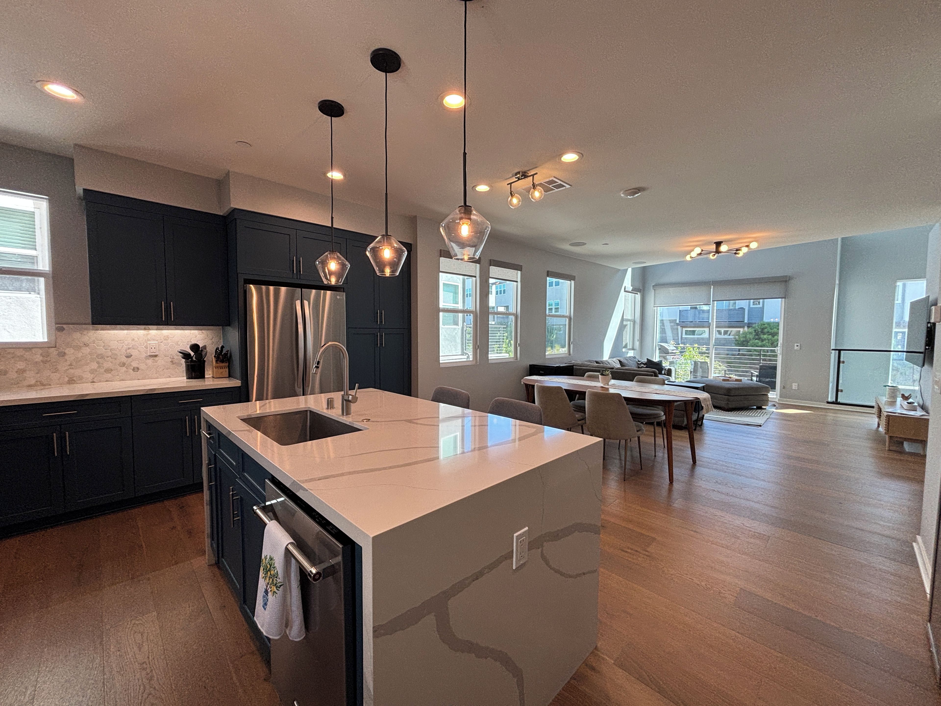 A modern kitchen with a central island, dark cabinetry, and pendant lighting.