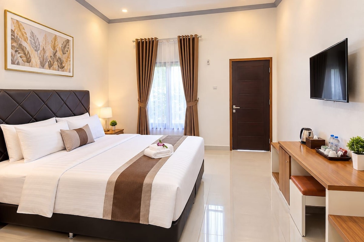 A hotel room with a bed, a desk, a TV, a door, and a window with curtains.