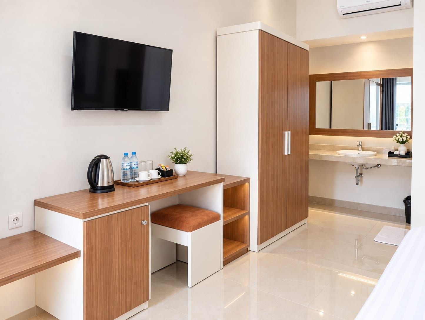 A modern hotel room with a flat-screen TV, a wooden desk with a cup holder, a small plant, and a bathroom with a sink and mirror.