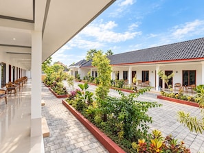 Un patio de hotel con piso de baldosas, mobiliario exterior y abundante vegetación.