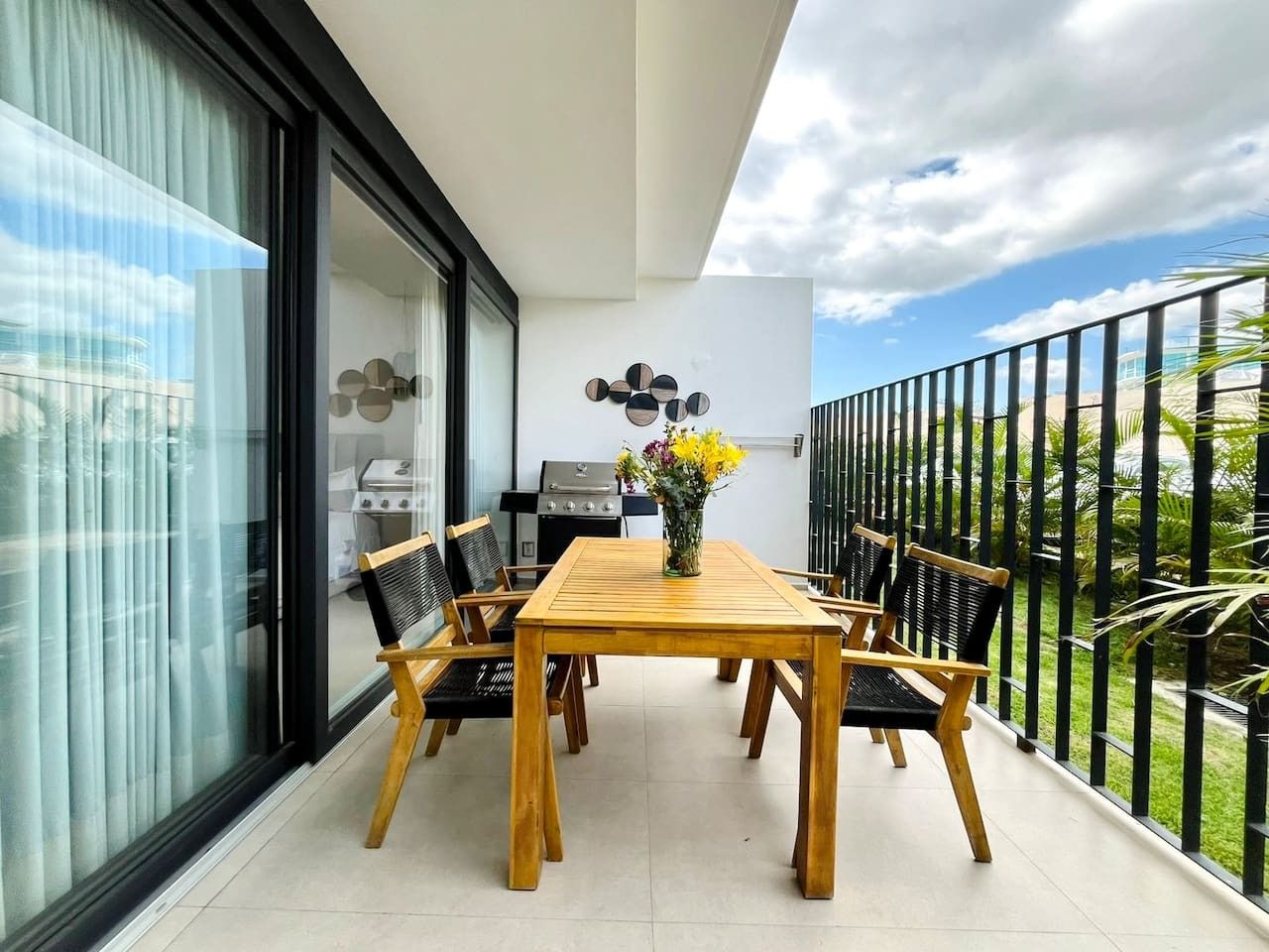 Un balcon avec une table et des chaises en bois, un barbecue et une vue sur le ciel et la verdure.