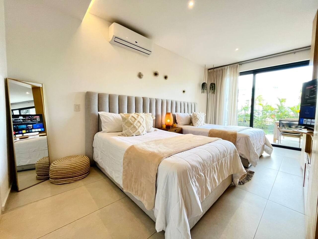A hotel room with two beds, a large mirror, a flat-screen TV, and a view of the outdoors.