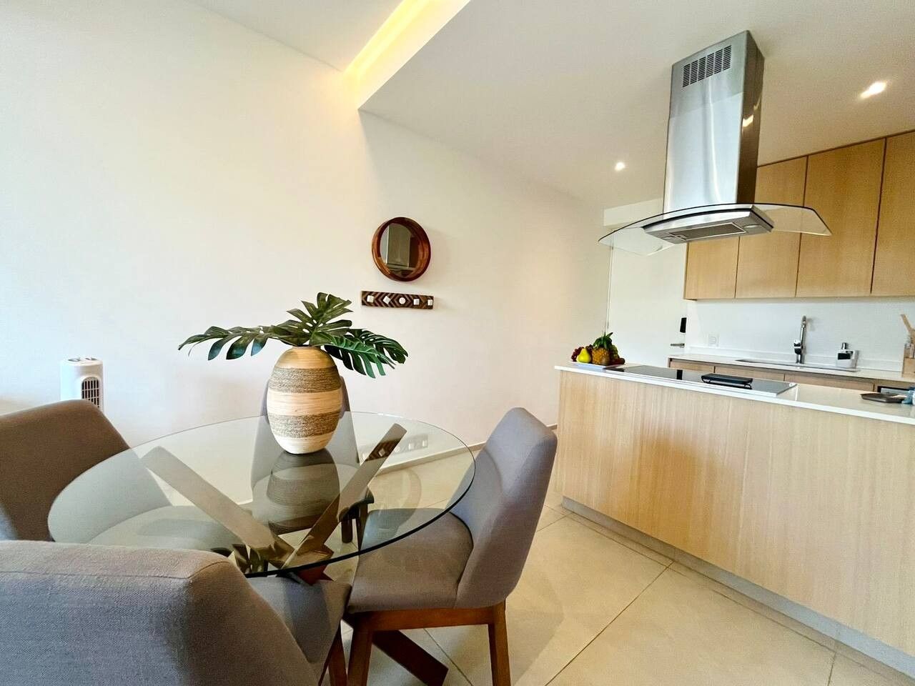 A modern kitchen with a central island, a dining area with a glass table, and a built-in stove.