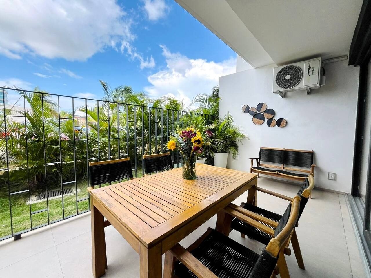 Un balcon avec une table et des chaises en bois, un pot de fleurs et un climatiseur fixé au mur.