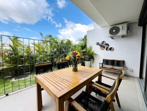 A balcony with a wooden table and chairs, a potted plant, and a wall-mounted air conditioning unit. - Groundfloor condo w/grill beach & pools Aria Ocean (Nuevo Vallarta)