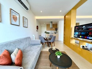 A modern living room with a grey sofa, a coffee table, and a TV on a wooden stand. - Groundfloor condo w/grill beach & pools Aria Ocean (Nuevo Vallarta)