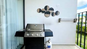 Uma varanda com churrasqueira, cilindro de gás e um objeto decorativo na parede.