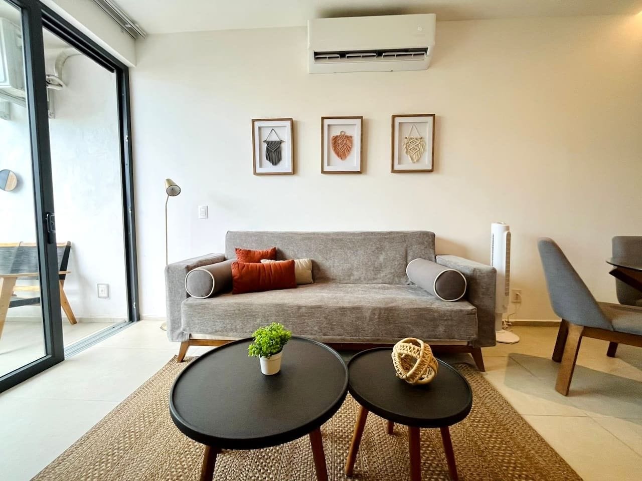 A modern living room with a grey sofa, two black coffee tables, and a small green plant. There are three framed wall art pieces above the sofa.