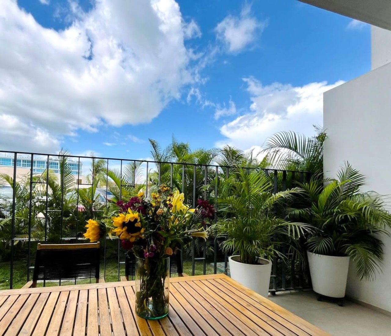 A wooden deck with a table and chairs, surrounded by potted plants and a vase of flowers.