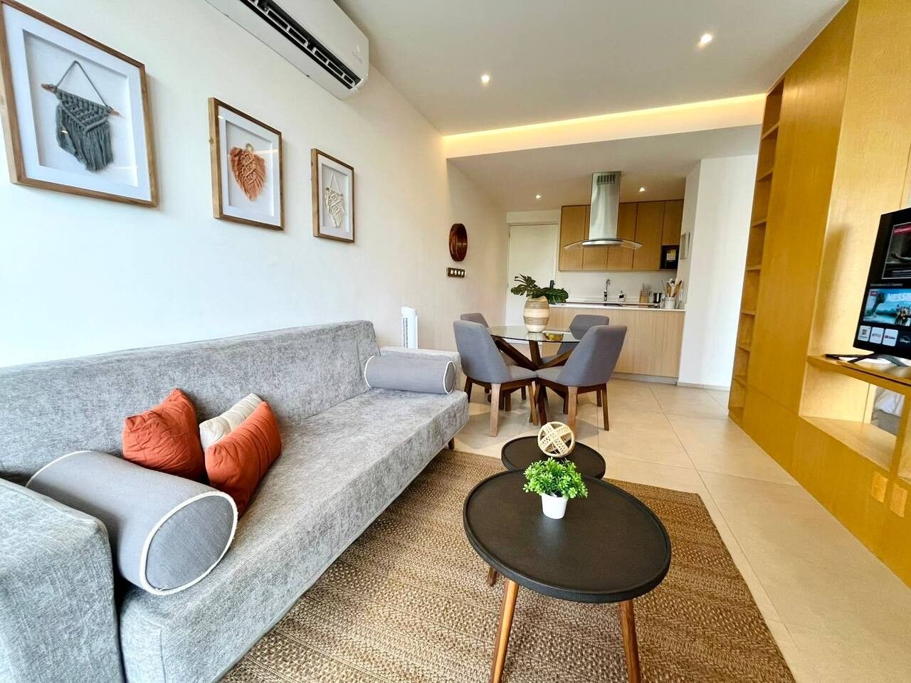 A modern living room with a grey sofa, a coffee table with a plant, and a dining area with chairs and a table.